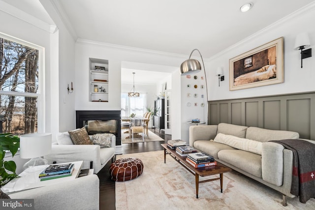 living room featuring a wainscoted wall, ornamental molding, light wood-type flooring, and a decorative wall