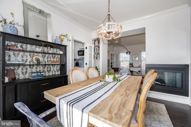 dining space with an inviting chandelier, ornamental molding, wood finished floors, and a glass covered fireplace