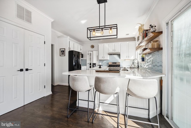 kitchen featuring stainless steel gas range oven, a peninsula, visible vents, light countertops, and crown molding