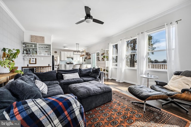 living area featuring a ceiling fan, baseboards, ornamental molding, and wood finished floors