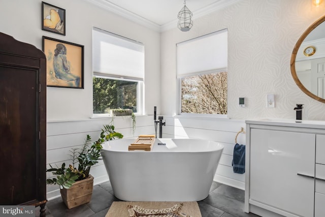 bathroom featuring wallpapered walls, wainscoting, a freestanding bath, vanity, and crown molding