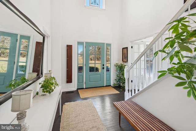 entryway featuring a towering ceiling, hardwood / wood-style flooring, stairs, and visible vents