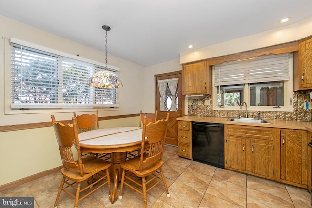 kitchen featuring a sink, black dishwasher, light countertops, hanging light fixtures, and brown cabinetry