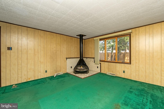 unfurnished living room featuring a wood stove, wood walls, carpet floors, and visible vents