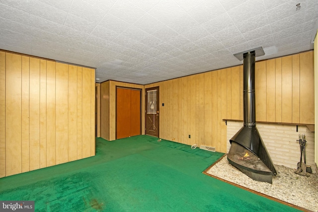 basement featuring carpet floors, a wood stove, visible vents, and wood walls