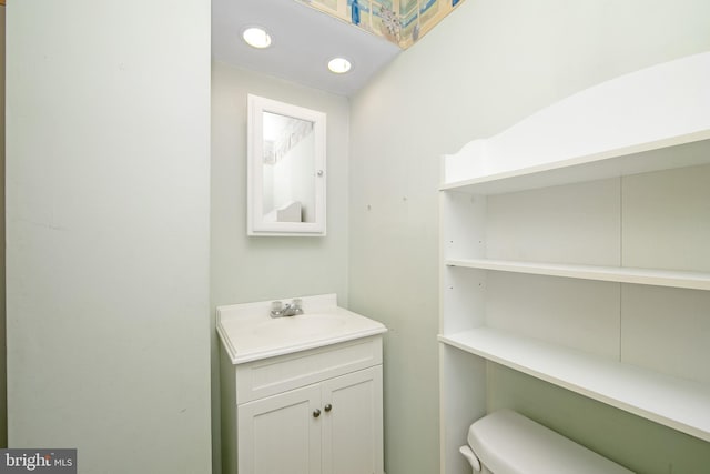 half bathroom featuring toilet, vanity, and recessed lighting