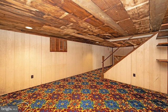 finished below grade area with carpet, wooden ceiling, wood walls, and stairway