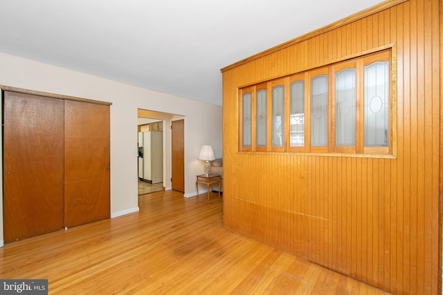 interior space with light wood finished floors, wooden walls, white refrigerator with ice dispenser, and a closet