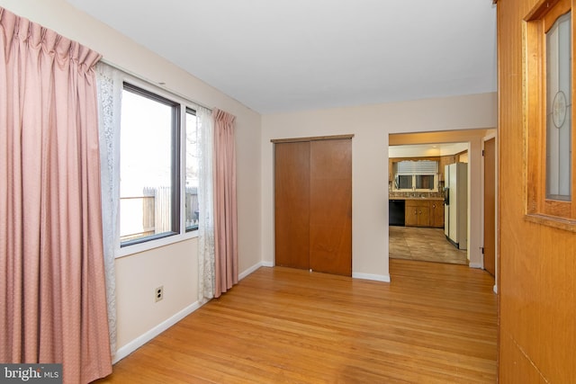 hall featuring light wood-style flooring and baseboards