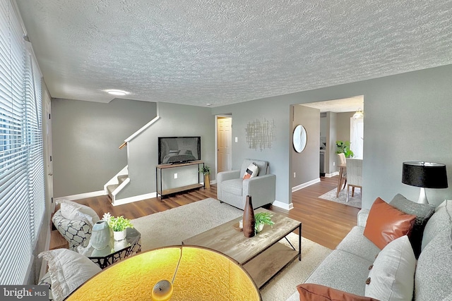 living room featuring a textured ceiling, stairs, baseboards, and wood finished floors