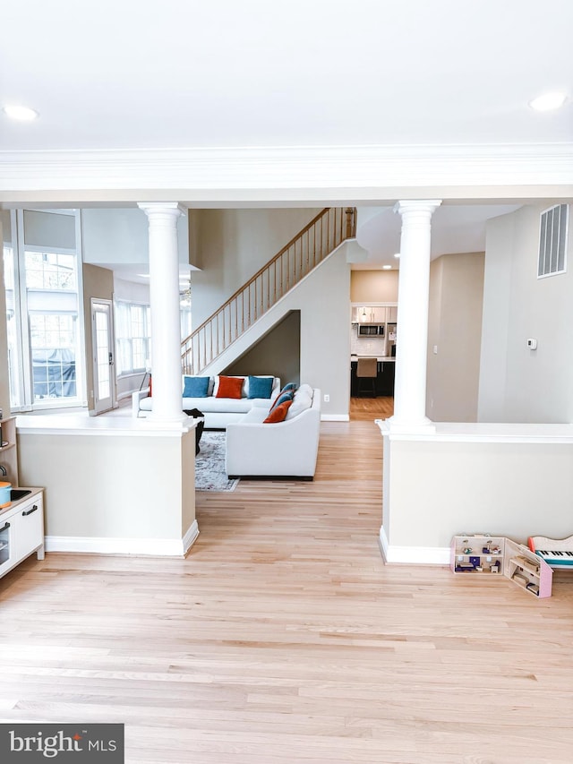 living room featuring decorative columns, visible vents, wood finished floors, and ornamental molding