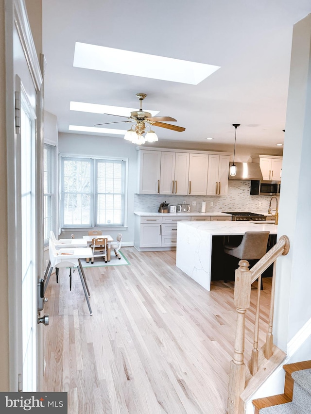 kitchen with a skylight, light wood finished floors, a breakfast bar area, tasteful backsplash, and stainless steel microwave