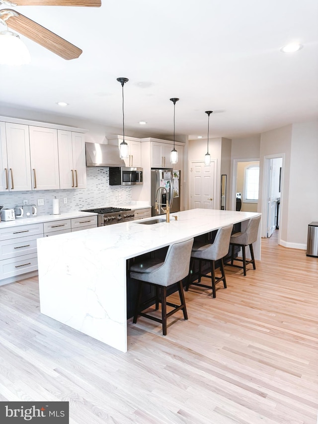 kitchen with tasteful backsplash, appliances with stainless steel finishes, a sink, a large island with sink, and wall chimney exhaust hood