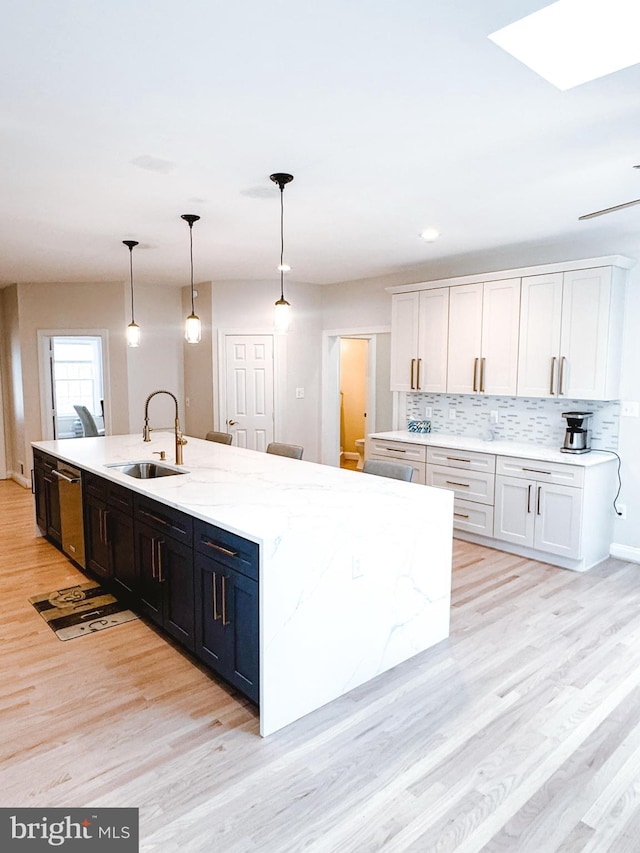 kitchen with tasteful backsplash, light wood-style flooring, decorative light fixtures, a sink, and stainless steel dishwasher