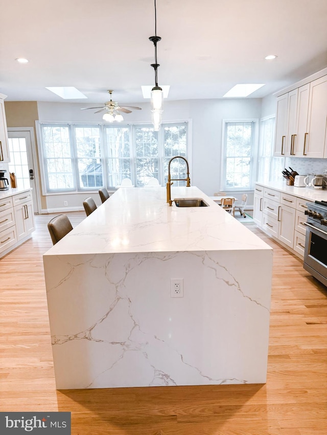 kitchen featuring a skylight, a center island with sink, light wood-style flooring, high end stove, and a sink