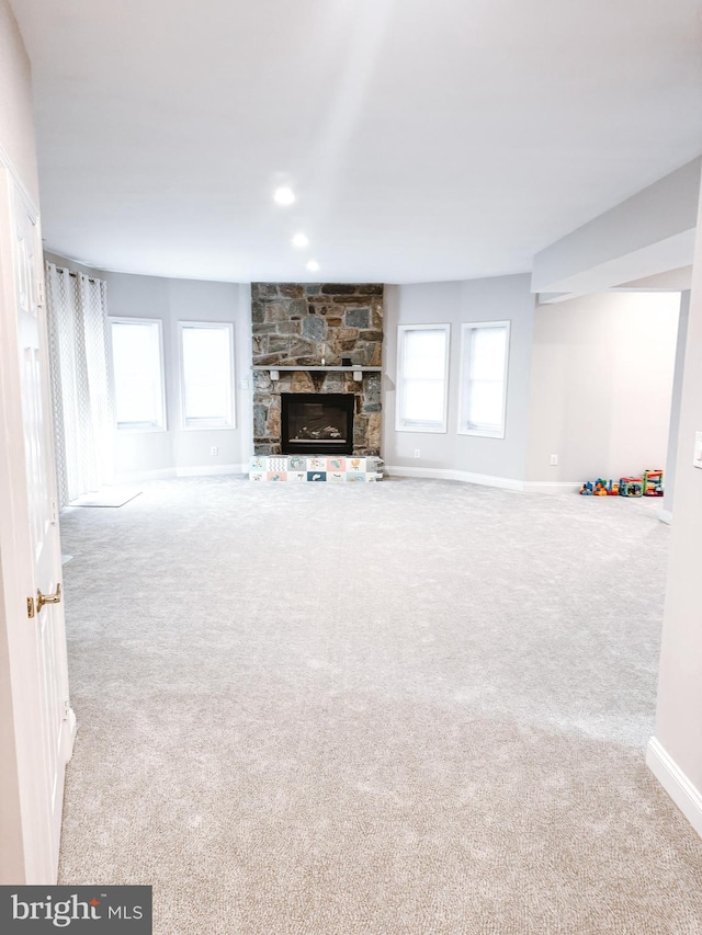 unfurnished living room with recessed lighting, carpet flooring, a stone fireplace, and baseboards