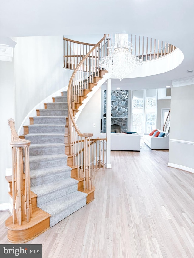 staircase with baseboards, a fireplace, wood finished floors, and a notable chandelier