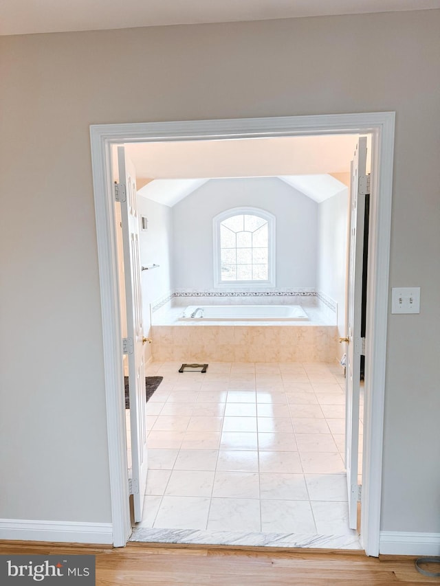 full bathroom with lofted ceiling, a garden tub, and baseboards