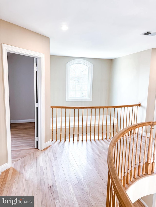 hallway featuring visible vents, baseboards, wood finished floors, and an upstairs landing