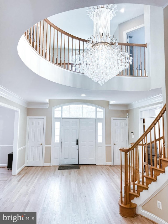 foyer featuring crown molding, stairway, a towering ceiling, wood finished floors, and a chandelier