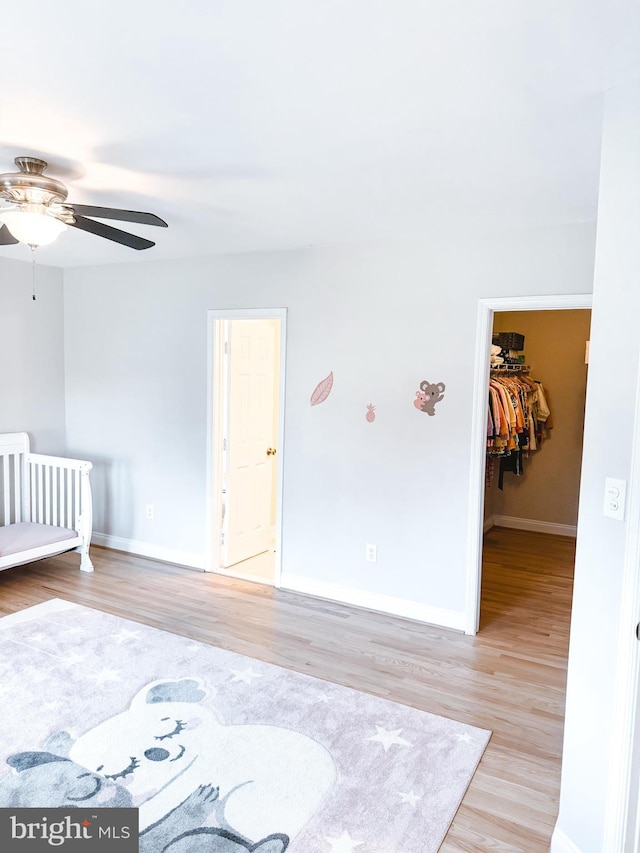 unfurnished bedroom with a walk in closet, baseboards, ceiling fan, and light wood finished floors