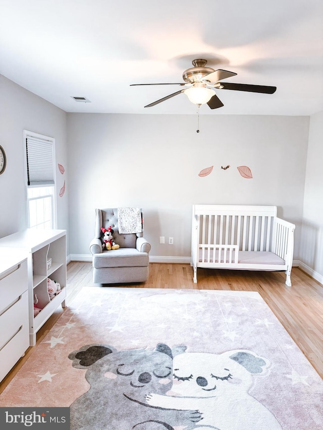 unfurnished bedroom with a nursery area, visible vents, baseboards, and wood finished floors