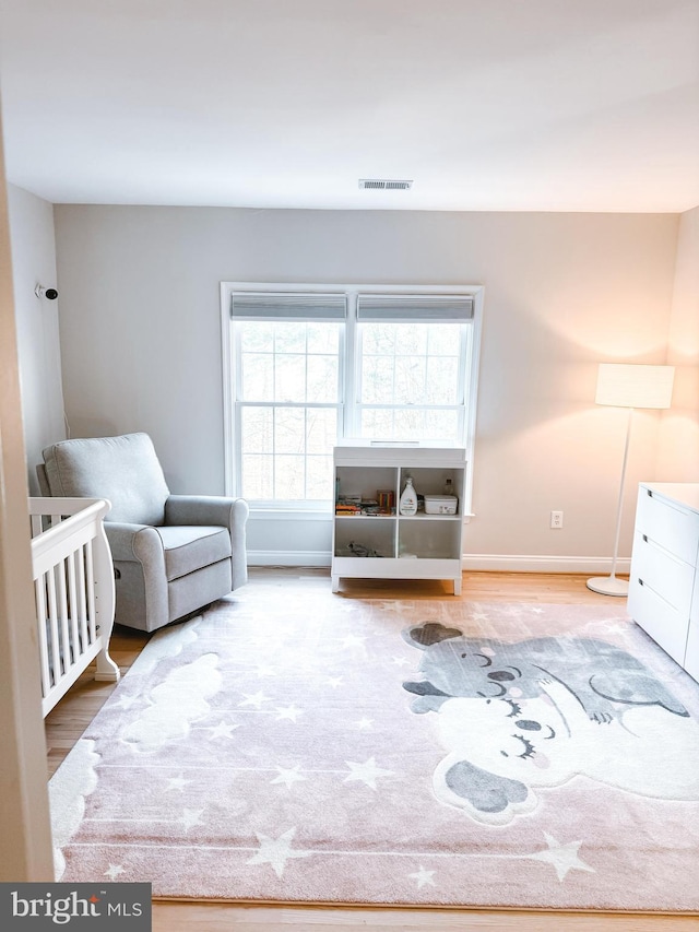 bedroom featuring a nursery area, baseboards, visible vents, and wood finished floors