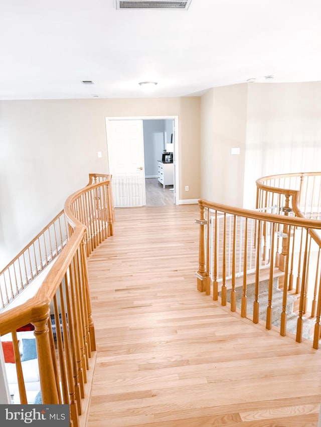 corridor with light wood-style floors, baseboards, visible vents, and an upstairs landing