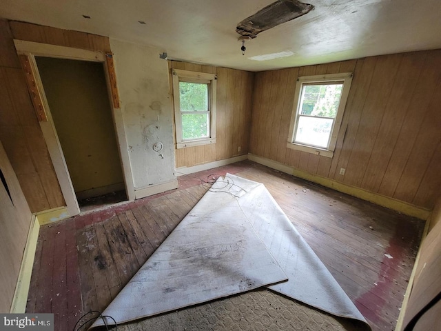 empty room with baseboards, light wood finished floors, wood walls, and a healthy amount of sunlight