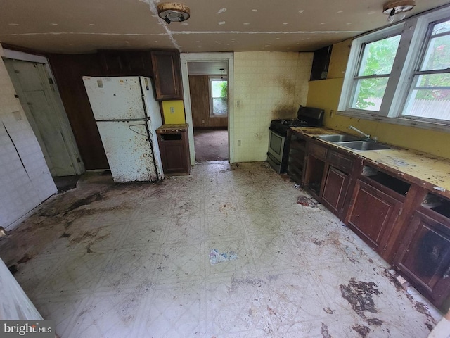 kitchen featuring a sink, range with gas stovetop, light countertops, freestanding refrigerator, and light floors