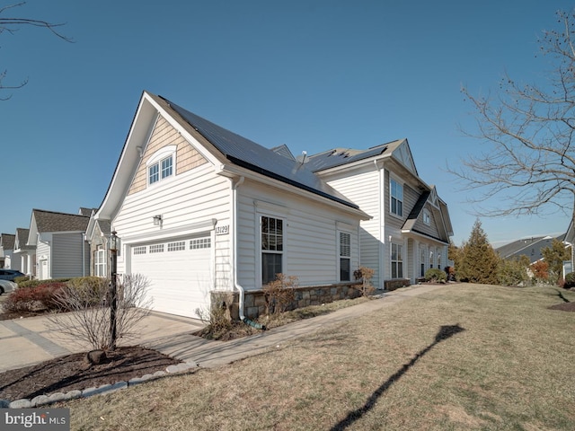 view of side of home with a garage, solar panels, stone siding, concrete driveway, and a lawn