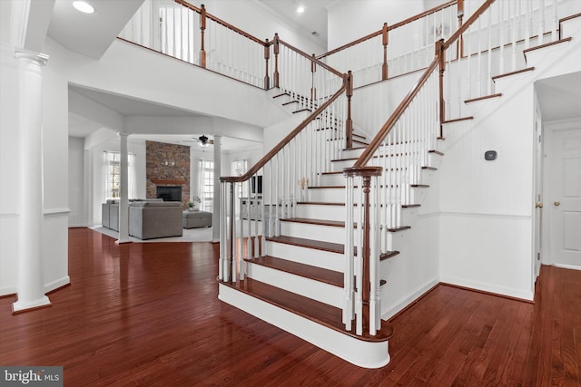 staircase featuring a fireplace, decorative columns, a high ceiling, wood finished floors, and baseboards