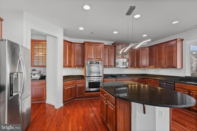 kitchen featuring recessed lighting, stainless steel appliances, a center island, dark wood finished floors, and glass insert cabinets