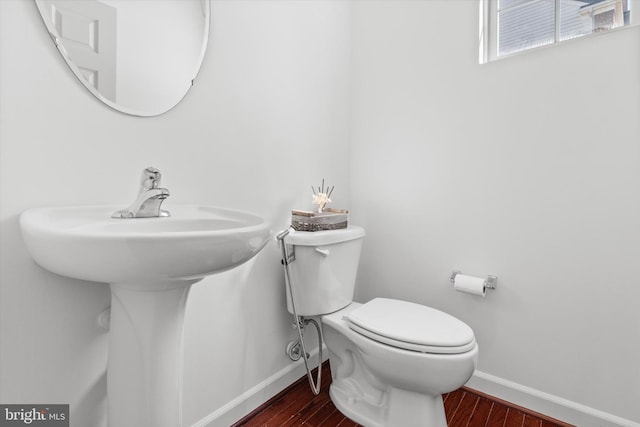 half bath with toilet, baseboards, and wood finished floors