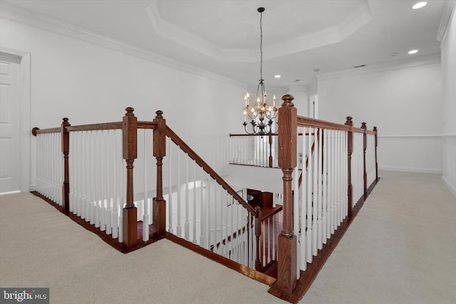 stairs with a chandelier, a raised ceiling, carpet flooring, and ornamental molding