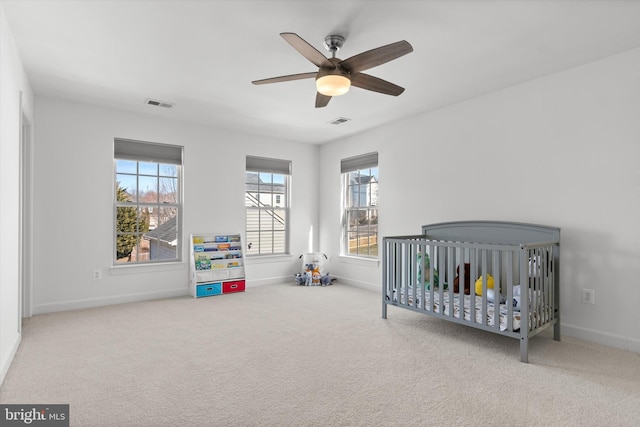 carpeted bedroom with a nursery area, ceiling fan, visible vents, and baseboards