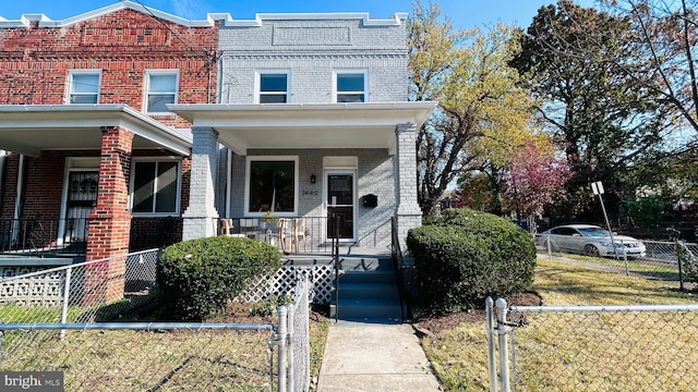 townhome / multi-family property with a fenced front yard, brick siding, and a porch