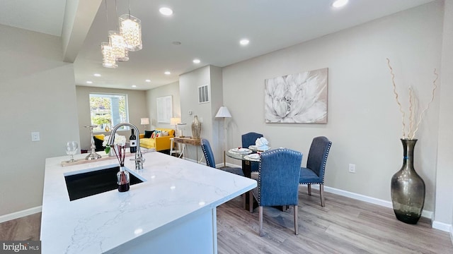 kitchen with baseboards, hanging light fixtures, light wood-style floors, a sink, and recessed lighting