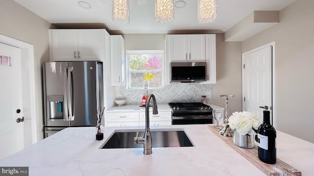 kitchen featuring light stone counters, stainless steel appliances, a sink, and decorative light fixtures