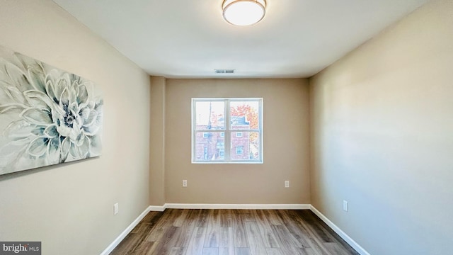 spare room with wood finished floors, visible vents, and baseboards