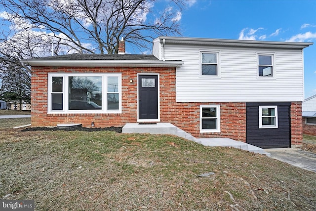 split level home featuring brick siding, a chimney, and a front yard