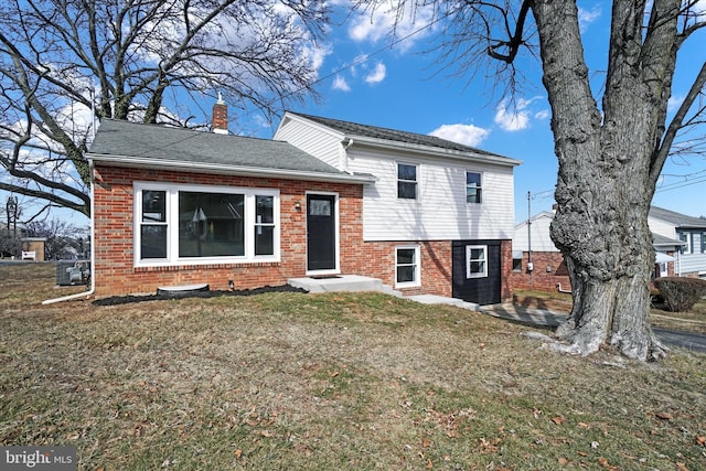 split level home featuring brick siding, a chimney, a shingled roof, and a front lawn