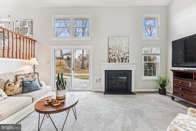 carpeted living area featuring a fireplace with flush hearth, a high ceiling, and baseboards