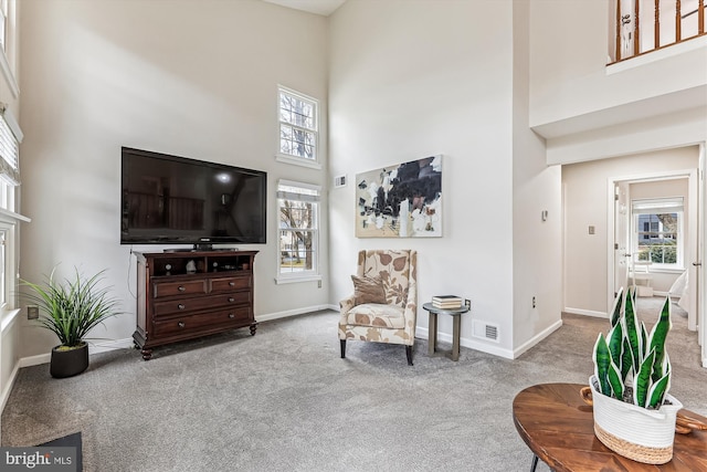 sitting room featuring a healthy amount of sunlight, visible vents, a towering ceiling, and carpet floors