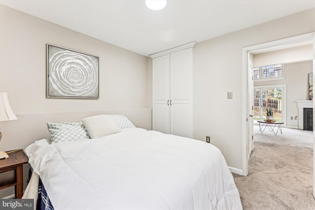 bedroom with light colored carpet, a fireplace, and baseboards