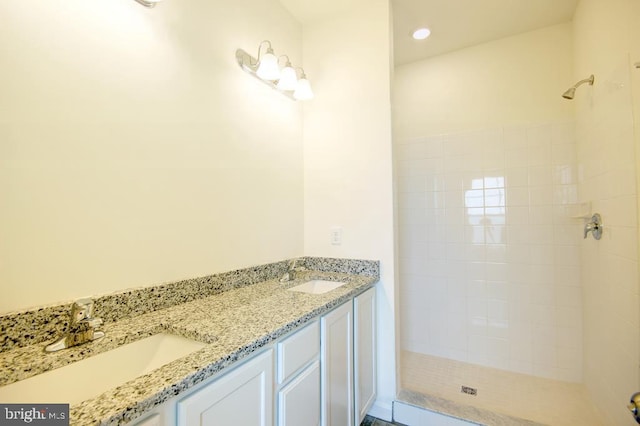 full bath featuring a sink, a tile shower, and double vanity