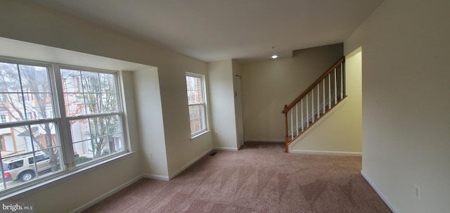 unfurnished room featuring light carpet, plenty of natural light, baseboards, and stairway