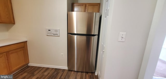 kitchen with dark wood-style floors, freestanding refrigerator, brown cabinetry, and light countertops