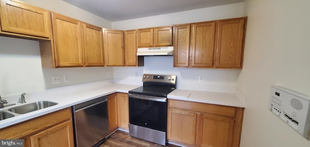 kitchen featuring brown cabinets, stainless steel appliances, light countertops, under cabinet range hood, and a sink