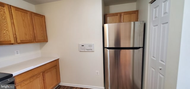 kitchen featuring brown cabinets, baseboards, light countertops, and freestanding refrigerator